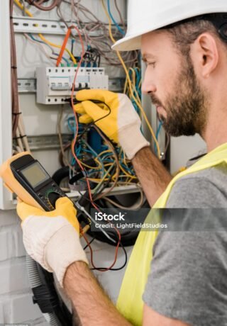 side view of bearded electrician checking electrical box with multimetr in corridor