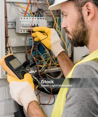 side view of bearded electrician checking electrical box with multimetr in corridor