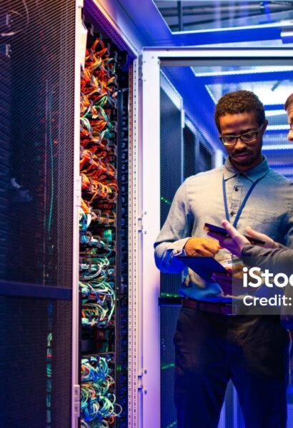 Two male IT engineers using digital tablet and smart phone in server room.