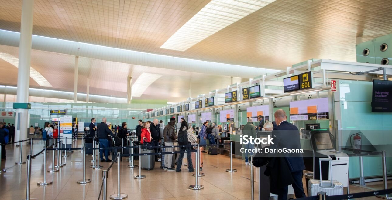 Travelers move through a spacious airport terminal toward the check-in and security areas.