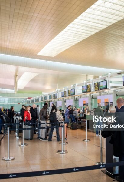 Travelers move through a spacious airport terminal toward the check-in and security areas.